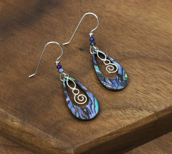 A pair of Celtic Spiral Paua Shell Earrings on a wooden table.