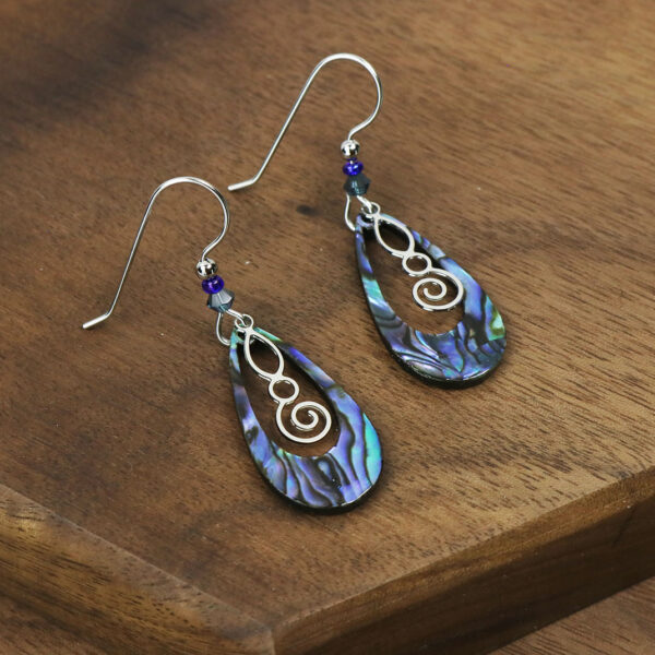 A pair of Celtic Spiral Paua Shell Earrings on a wooden table.