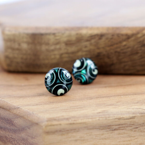 A pair of Triskelion Spiral Paua Shell Earrings on a wooden table.