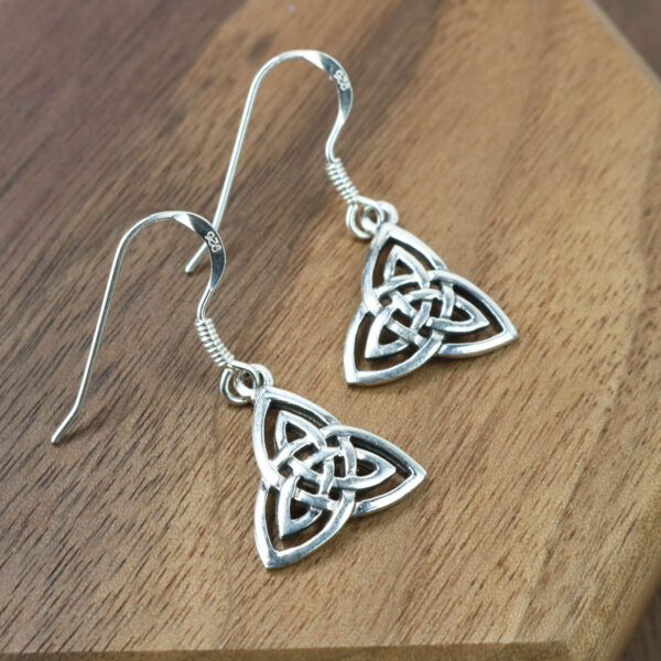 A pair of sterling silver Trinity Knot Earrings on a wooden table.