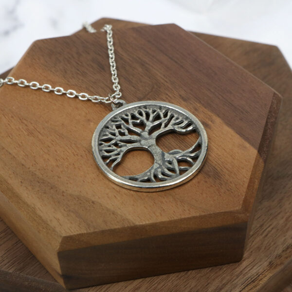 An Amethyst Celtic knot necklace featuring a silver tree of life pendant rests gracefully on a wooden table.
