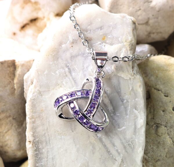 An amethyst trinity necklace on a rock, complemented by Celtic Knot Emerald Earrings.