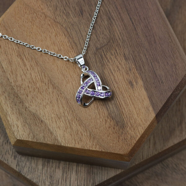 An Amethyst Celtic Knot Necklace with a Celtic knot pendant on top of a wooden table.