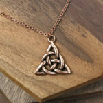 An Amethyst Celtic Knot Necklace with an amethyst pendant, resting on a wooden table.
