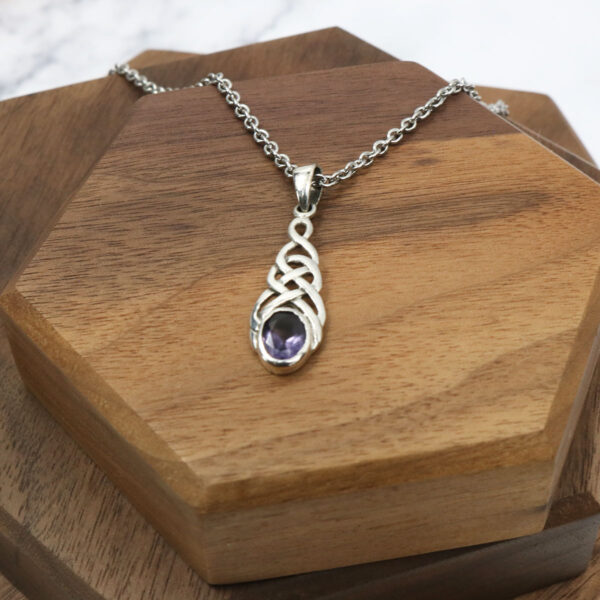 An Amethyst Celtic Knot Necklace featuring a stunning amethyst pendant elegantly placed on a wooden table.