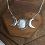 An Amethyst Celtic Knot necklace with three moon phases on top of a wooden table.