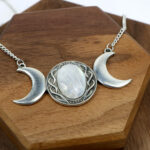 An Amethyst Celtic Knot Necklace adorned with three moon phases, crafted on top of a wooden board.