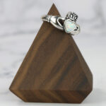 A two tone opal claddagh ring on a wooden base with a Two Tone Eternity Knot Band.