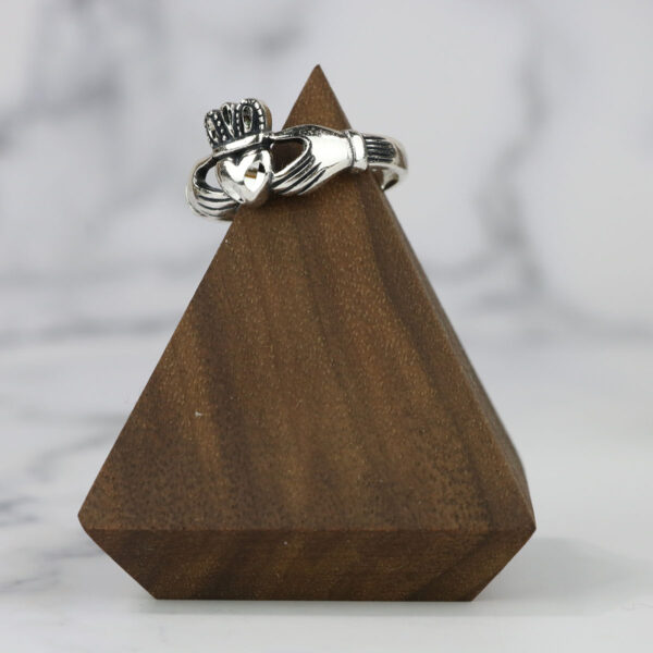 A claddagh ring with a Two Tone Eternity Knot Band, displayed on a wooden stand.