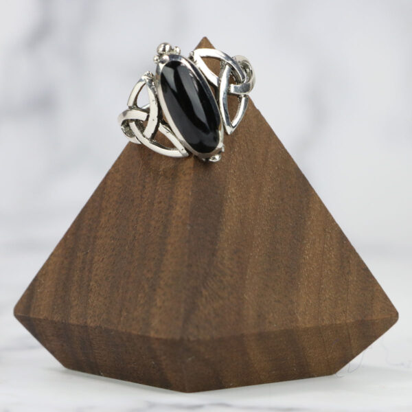 A Black Onyx Trinity Celtic Knot Ring adorned with a Celtic knot design, displayed elegantly on a wooden stand.