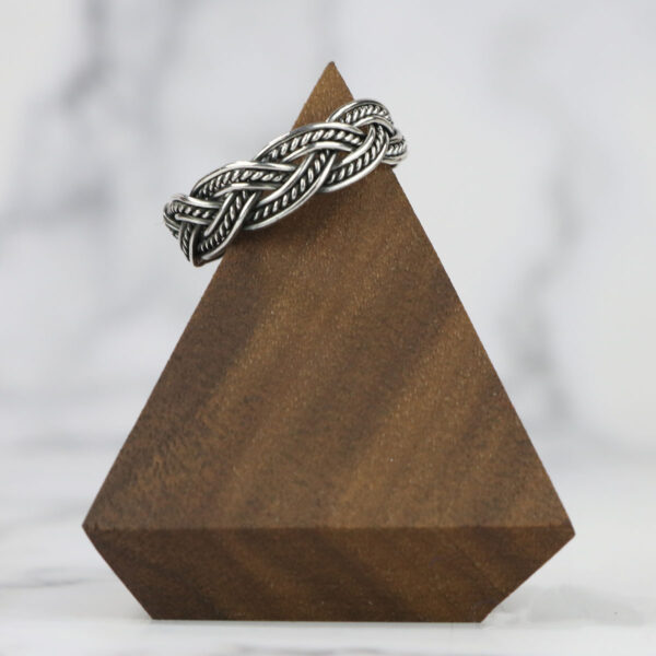 A Two Tone Eternity Knot Band silver ring on top of a wooden triangle.