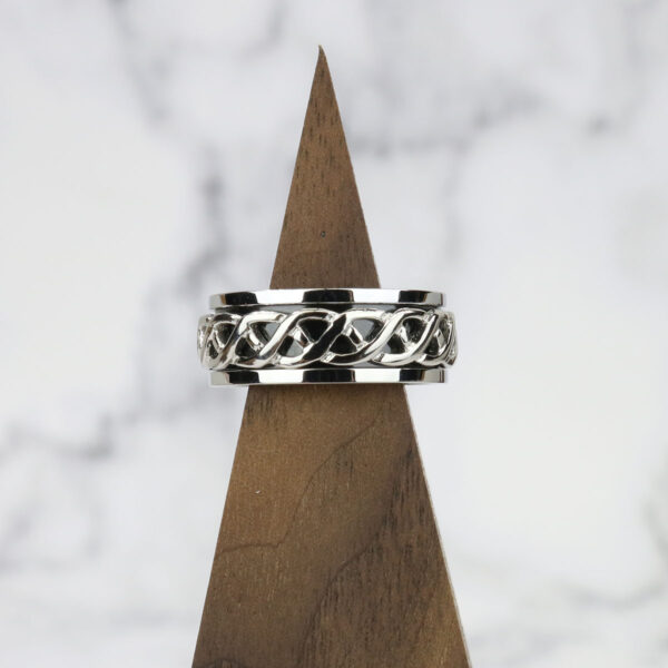 A Celtic Knot Spinner Ring-Size 13 with an intricate Celtic knot design on top of a wooden base.