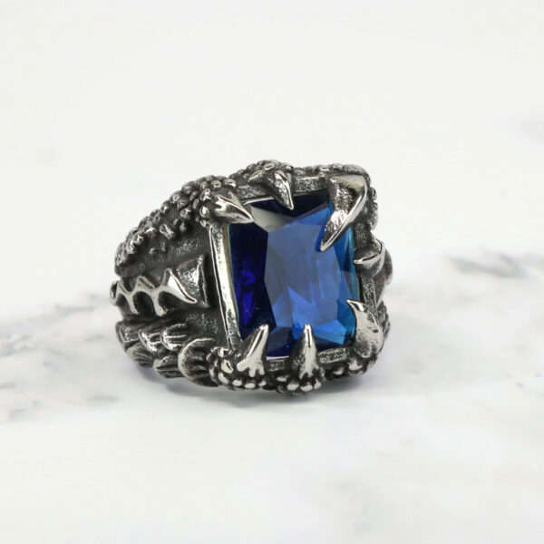 A Dragon Claw Stainless Steel Ring with a blue sapphire encased in silver.