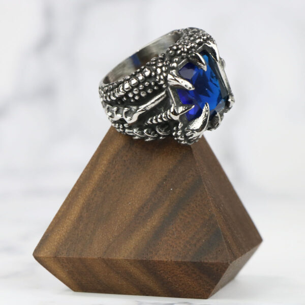 A Dragon Claw Stainless Steel Ring with a blue stone on top of a wooden stand.