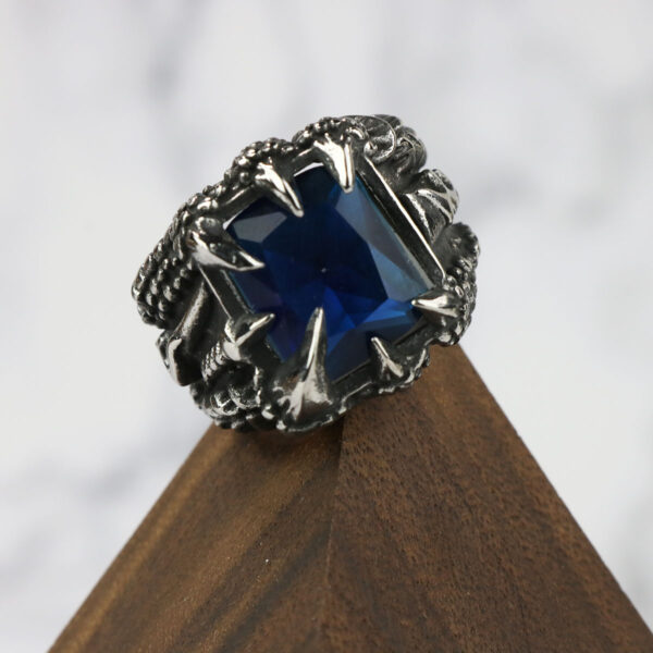 A silver Dragon Claw Stainless Steel Ring with a blue sapphire on top.