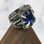 A Dragon Claw Stainless Steel Ring with a blue sapphire on top.