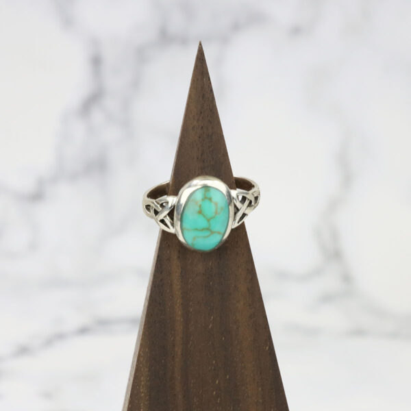 A silver *Turquoise Triquetra Ring* with a turquoise stone on top.