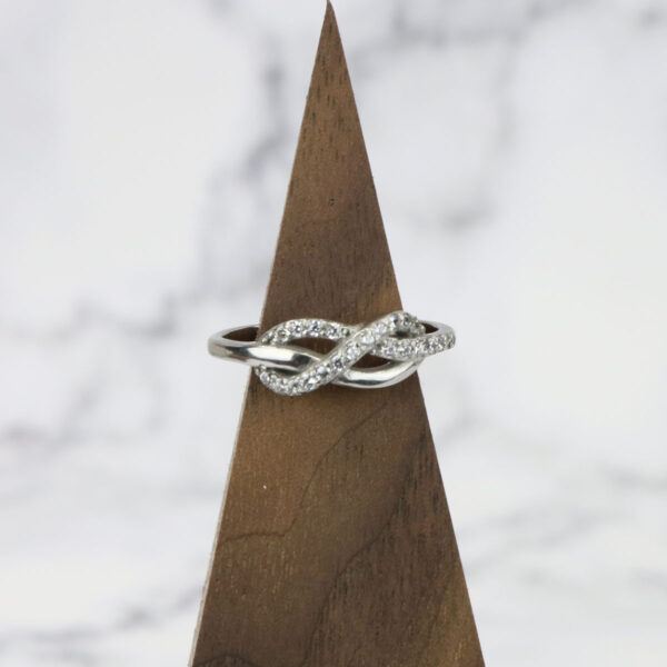 An Infinity Knot Ring with diamonds on top of a wooden base.