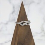 An Infinity Knot Ring with diamonds atop a wooden base.