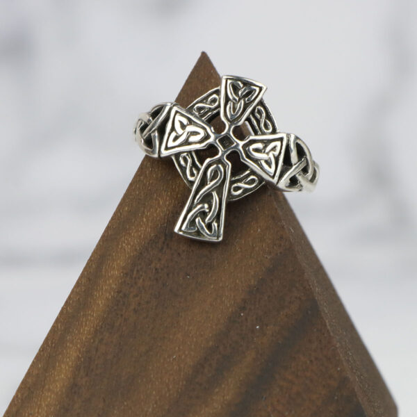 A sterling silver celtic cross ring with a Two Tone Eternity Knot Band, elegantly displayed on top of a wooden block.