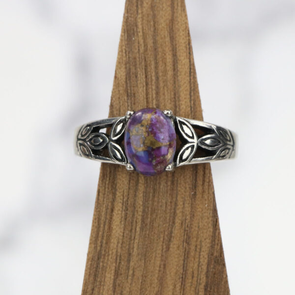 A Purple Mohave Turquoise Triquetra Ring atop a wooden base.
