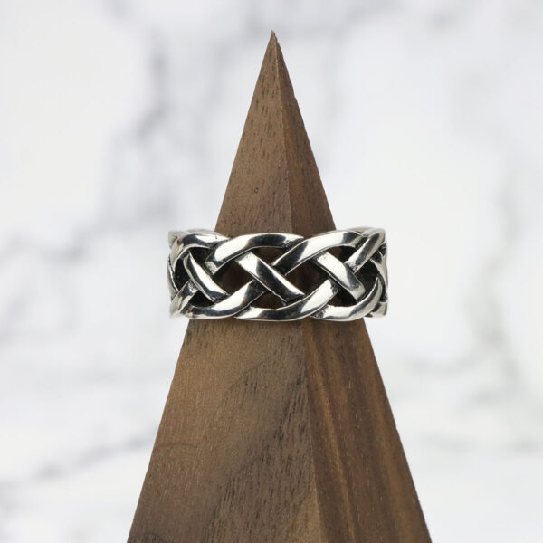An Interlacing Endless Knot Ring with a Celtic design on top of a wooden base.
