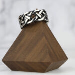 An Interlacing Endless Knot Ring displayed on a simple wooden stand.