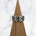 A silver Interlacing Endless Knot Ring with an interlacing braided pattern on top of a wooden base.