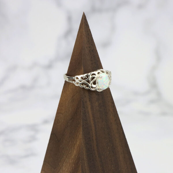 A white opal ring with a Two Tone Eternity Knot Band on top of a wooden base.