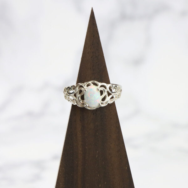 A white opal ring with a Two Tone Eternity Knot band, resting on top of a triangle.