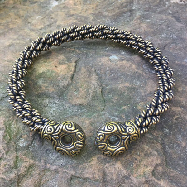A Chieftains Torc Extra Heavy Braid, a gold and black braided bracelet, rests on a rock.