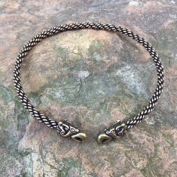 The Celtic Griffin Neck Torc rests gracefully on a rock, its intricate design combining threads of gold and black in a stylish braided choker.