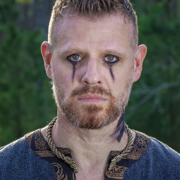 A bearded man adorned with viking tattoos, while wearing a Celtic Horse Neck Torc around his neck.