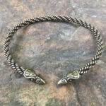 A Celtic Raven Neck Torc bracelet on a stone surface.