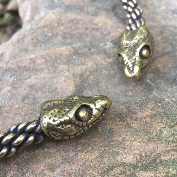 A pair of Celtic Snake Torc - Medium Braid bracelets on a rock.