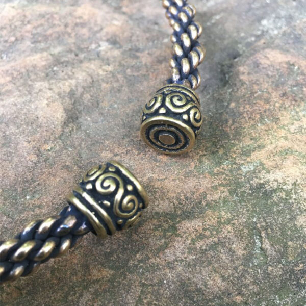 A pair of Celtic Spiral Torc - Medium Braid beads on a rock.