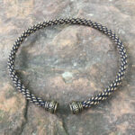 A black and gold Celtic Spiral Torc - Medium Braid choker on a rock.