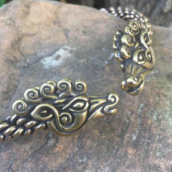 A pair of brass bracelets with a dragon head and Celtic Stag Neck Torc on them.