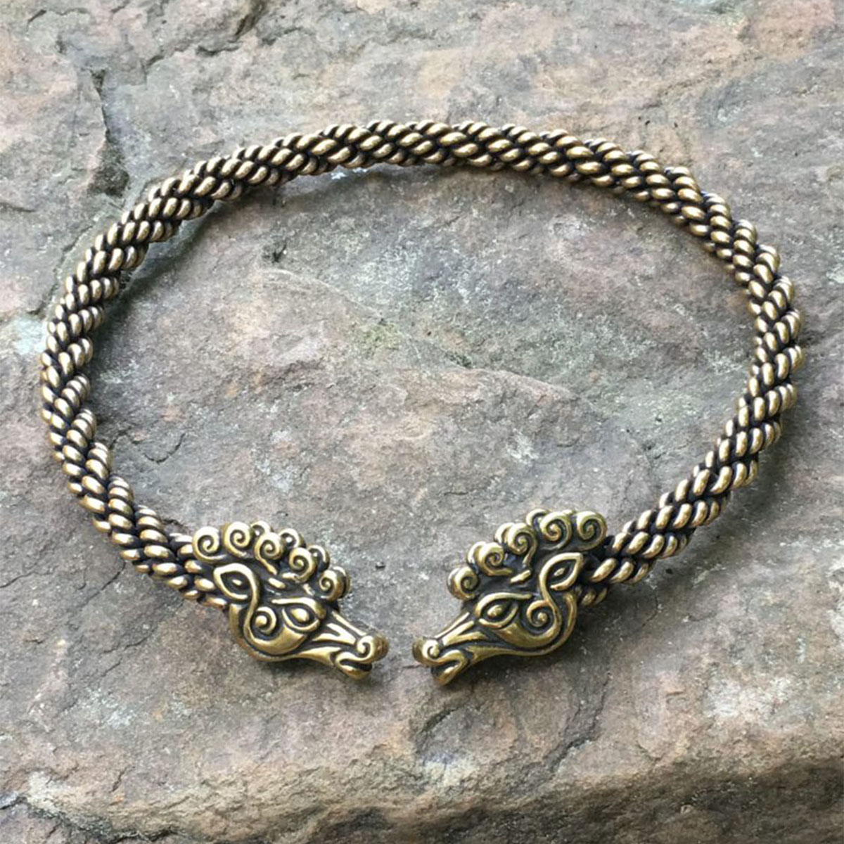 Two Celtic Stag Neck Torc bracelets on top of a rock.