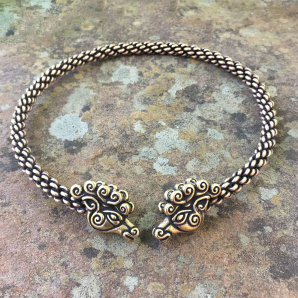 Two Celtic Stag Neck Torc bracelets on a stone surface.