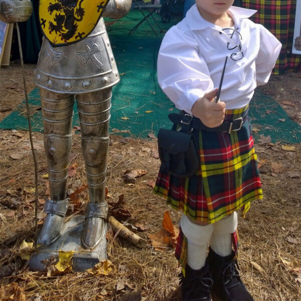 A young boy in a Medium Ancient Kid Kilt standing next to a medium-sized statue.