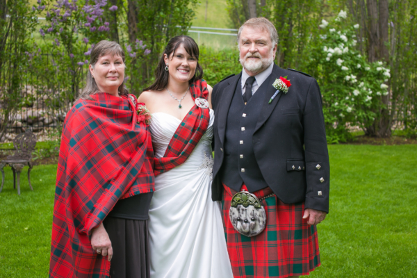A bride and groom wearing kilts and posing for a photo with a Light Weight Premium Wool Tartan Sash.
