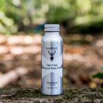 A bottle of Nutdust Sampler Pack of 3 beard oil sitting on a log in the woods.