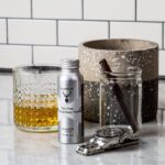 A Nutdust Sampler Pack of 3, a glass, and a bottle of whiskey.