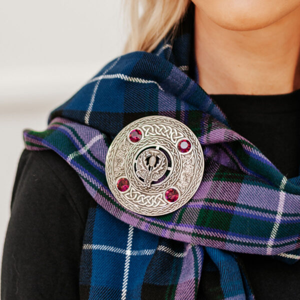 A woman wearing a scottish tartan scarf with a brooch.