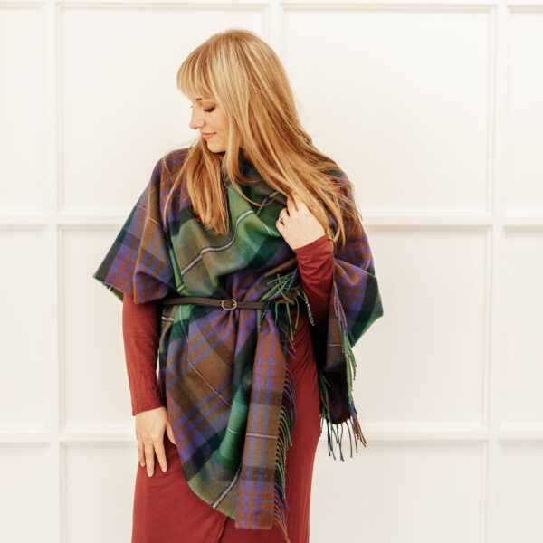 A woman wearing a Scottish Lambswool Tartan Poncho standing in front of a white wall.