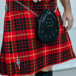 A man wearing a red and black tartan kilt - a Quality Wool Blend Kilt with Matching Tartan Flashes and FREE Kilt Hanger.