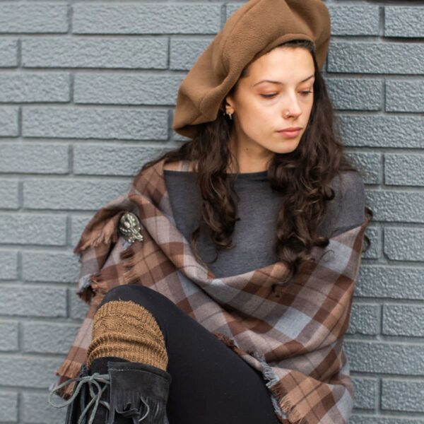 A woman wearing a Tartan Scarf - 13oz Premium Wool and black boots leaning against a wall.