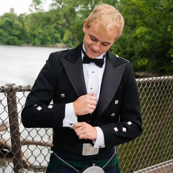 A young man in a kilt is adjusting his tie.