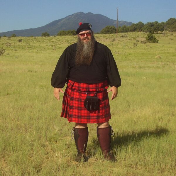 A man in a Welsh Tartan Medium Weight Premium Wool Phillabeg kilt standing in a field.